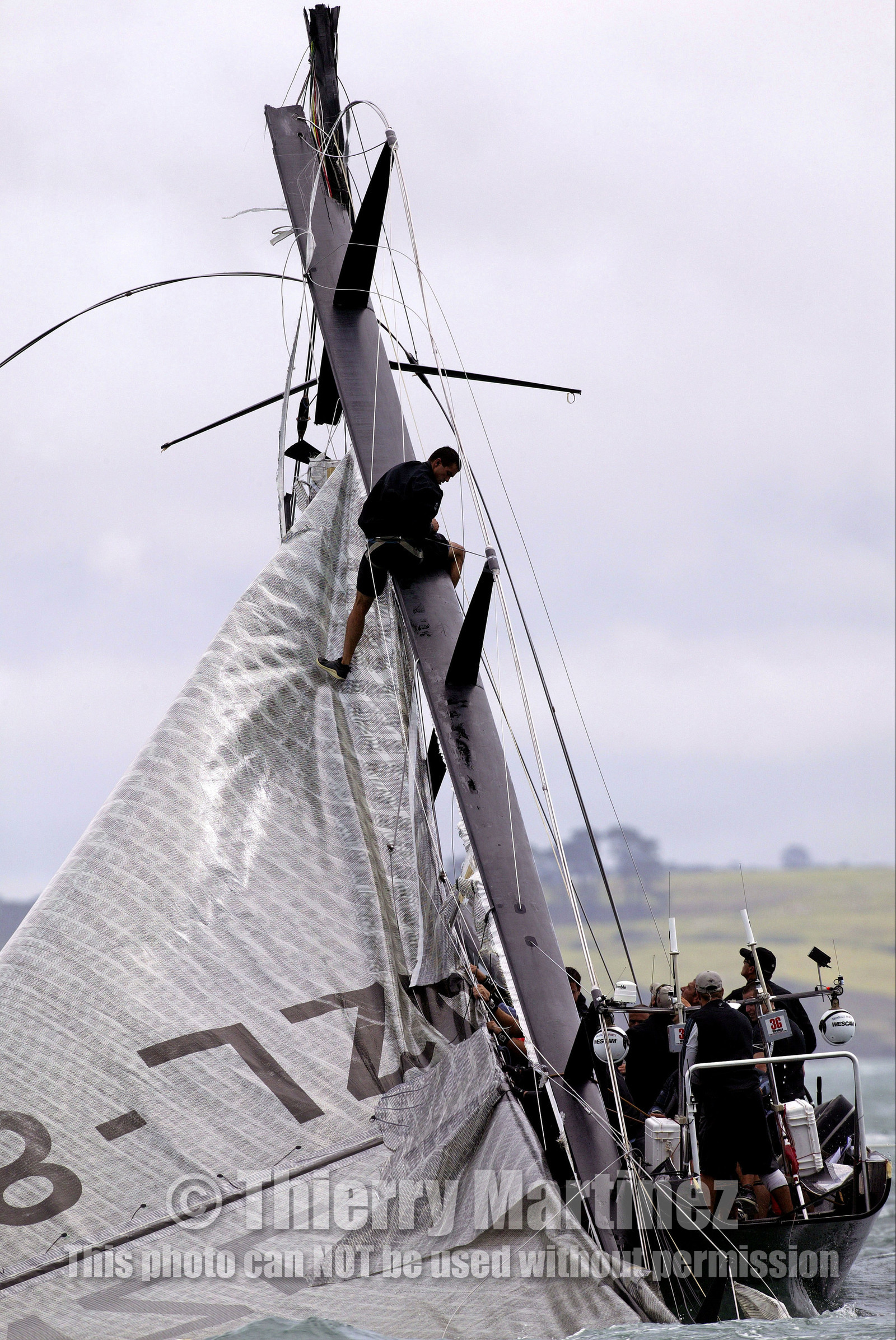 03_0257D ©Th.Martinez - Auckland (NZ) . America's Cup 2003. 28th February 2003. Day 4 .Alinghi (SUI 64) vs Team NZ (NZL 82) .Team NZ's boat dismast 57 minutes after the start in only 18 knots of windwith a swell of 1.5 m. Team NZ crew trying to take off the mainsail  on the broken mast. Alinghi is leading Team NZ  4-0 after 4 races..